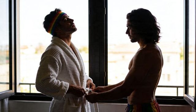 Intimate gay couple adjusting robe on sunlit urban balcony sharing quiet morning together