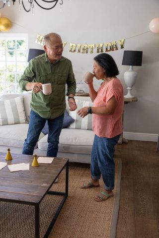 Mature chinese couple celebrating birthday at home holding mugs and laughing