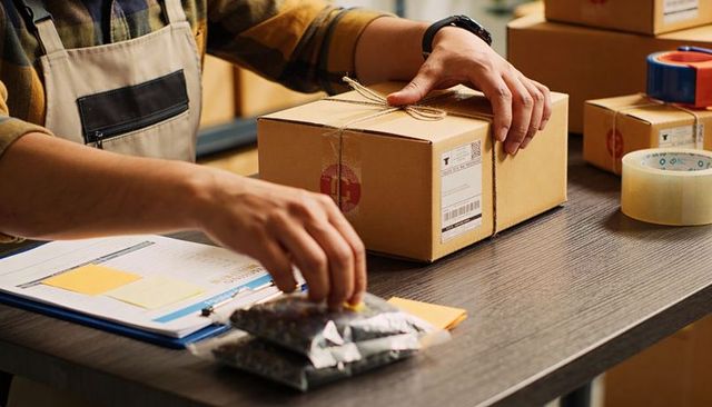 Hands tying twine around parcel on workbench for small business shipping and packaging