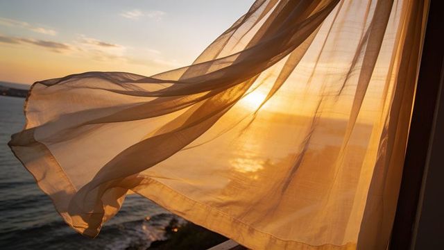 Sheer curtain billowing over golden sunset ocean from seafront balcony, warm coastal light