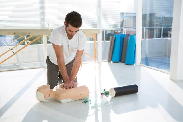 Paramedic practicing CPR on a dummy in a bright clinic. Useful for illustrating medical training, emergency preparedness, healthcare education, and professional skill development.