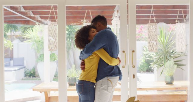 Young interracial couple is embracing in a warmly lit home interior. The scene shows affection and happiness. This image can be used for promoting family values, articles on relationships, or advertisements focused on lifestyle and home living.