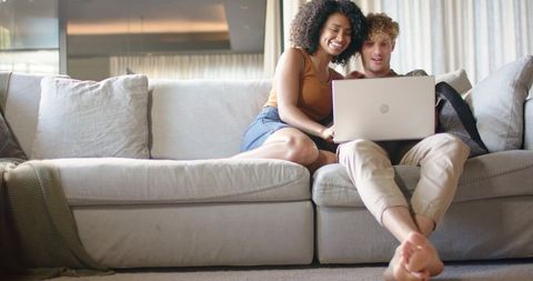 Couple relaxing on sofa while browsing laptop in cozy neutral-toned living room