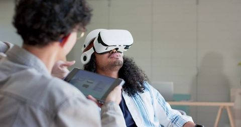 Diverse team testing vr headset in modern workspace, collaboration using tablet and laptop