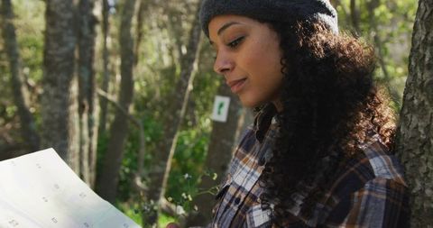 Holding map and examining trail: woman wearing plaid shirt and beanie in forest