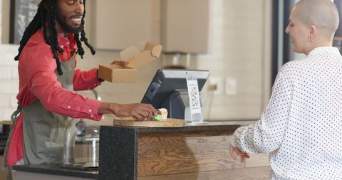 African american barista serving takeout at cafe counter with qr payment sign