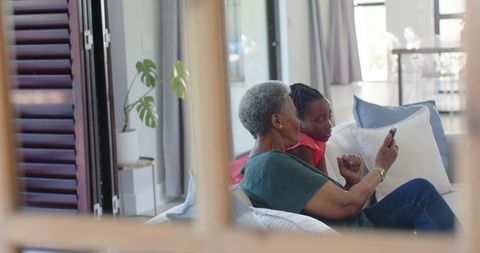 African grandmother and granddaughter sharing smartphone moments on cozy living room sofa