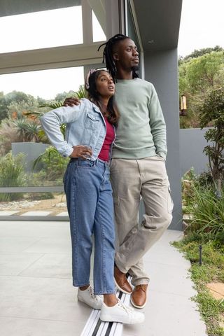 Relaxed multicultural couple standing on modern patio gazing at lush garden