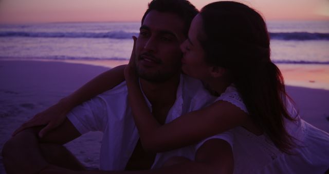 Biracial couple enjoys a romantic moment at sunset on the beach, with copy space. Gentle waves and vibrant skies provide a serene backdrop for their affectionate embrace.