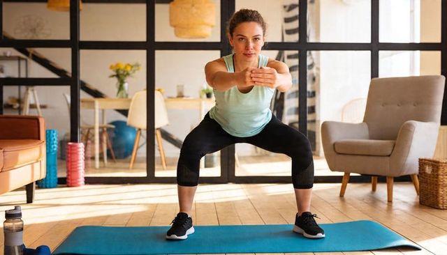 Performing wide squat during at-home workout on mat in bright modern living room