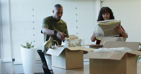 African american coworkers unpacking boxes and bubble wrap during office move and staging