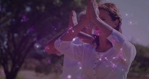 Woman practicing yoga in sunlit field holding palms together with purple bokeh meditation