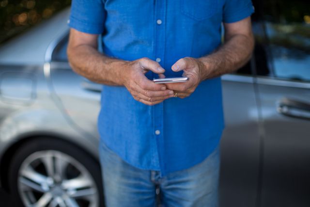 Mid section of man using mobile phone by car parked on road