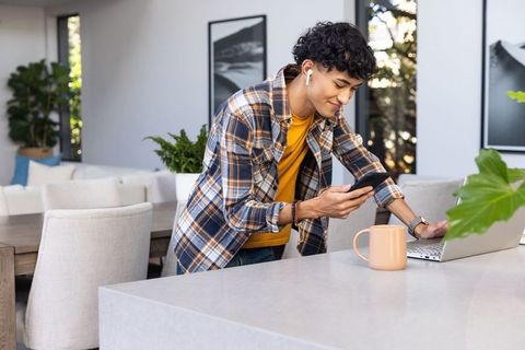 Young Adult Multitasking with Laptop and Smartphone in Modern Kitchen