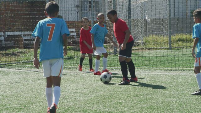 Two teams of multi-ethnic children are playing soccer on a green football pitch on a sunny day. They are actively engaging in passing and shooting the ball, showcasing teamwork and sportsmanship. This video can be used for promoting youth sports programs, physical fitness activities for kids, teamwork and social interaction among children, or advertisements for soccer-related products or youth sports events.