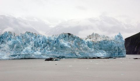 Blue Glacier Front Looming over Calm Water with Foggy Mountain Backdrop