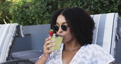 African american woman sipping lime drink poolside wearing crochet coverup sunglasses