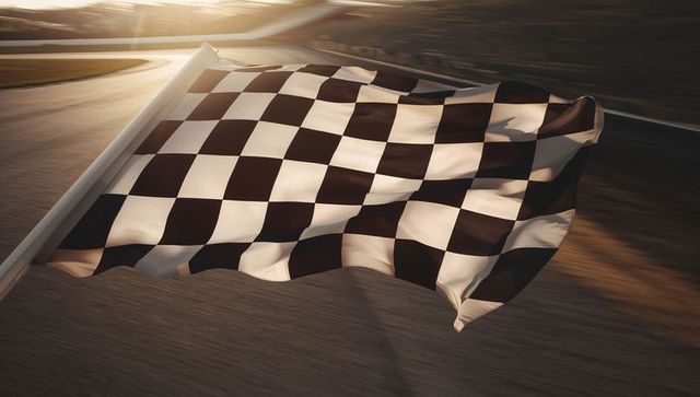 Flapping checkered racing flag waving at finish line over racetrack during golden hour