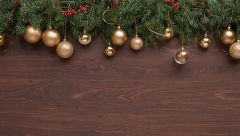 Elegant gold christmas garland featuring red berries and baubles on dark wood backdrop