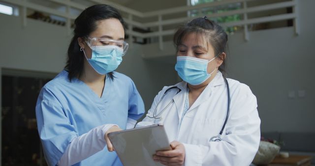 Two female healthcare workers are discussing medical records in a hospital, wearing protective masks. This image showcases medical professionals collaborating and verifying information. It can be used to depict teamwork, professionalism, and healthcare environments, suitable for healthcare-related websites, medical promotional materials, and educational content.