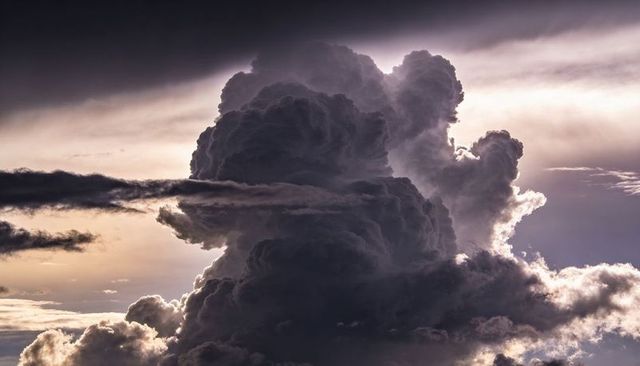 Towering cumulonimbus sculpting dramatic backlit thunderhead at dusk with glowing rimlight