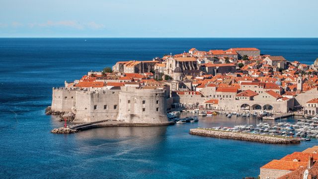 Aerial view of Dubrovnik Old Town showcasing historic buildings, harbor filled with boats, blue sea meeting the fortified walls. Ideal for travel advertisements, promotional materials, or articles featuring travel destinations and cultural heritage sites. Also suitable for educational purposes highlighting architecture and history.