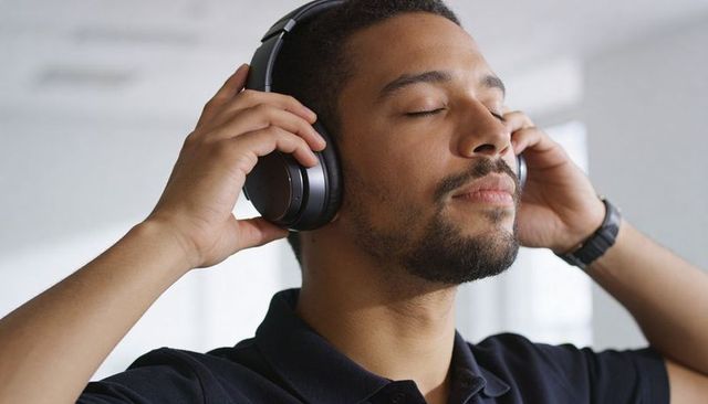 Man adjusting over-ear headphones enjoying music and relaxing with eyes closed