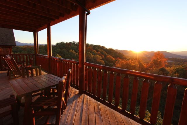 Wooden porch of a cabin overlooking a mountainous forest area at sunset. Warm sunlight enhances the natural beauty, creating a serene atmosphere. Ideal for travel brochures, vacation rentals advertising, outdoor lifestyle blogs, and nature-focused publications.