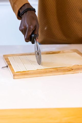 African american hand cutting puff pastry strips with rotary cutter on bamboo board
