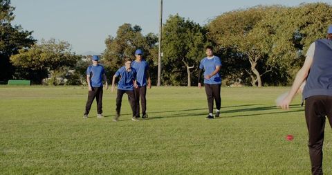 Youth team practicing throwing and fielding drills on sunny park grass with bright red ball