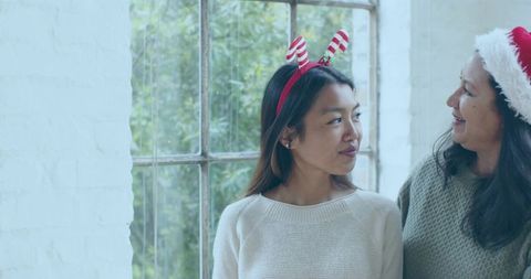 Mother and daughter sharing warm holiday moment by window wearing festive hats