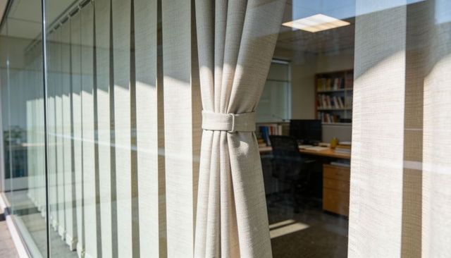 Sunlit pleated curtain with tie-back framing modern office interior through glass window