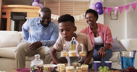 African American family celebrating birthday with child blowing out cupcake candles