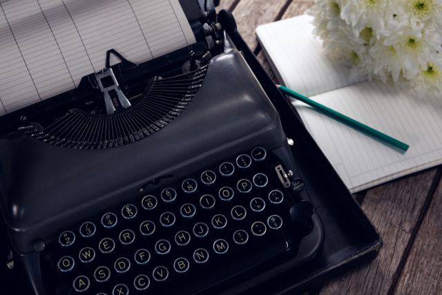 Close-up of vintage typewriter, diary and flowers on wooden table