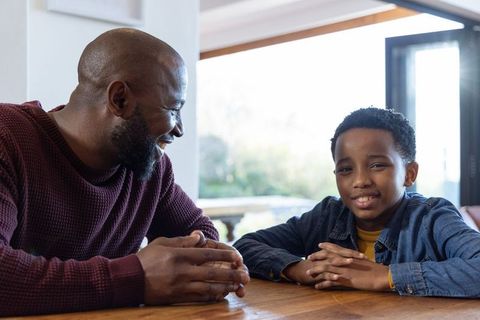 African american father and son sharing warm laugh at wooden table near glass door
