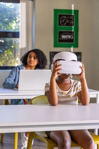 African american child experiencing virtual reality in classroom with educator and laptop