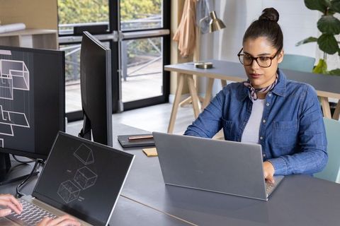 Woman working at modern shared desk using laptop and monitors in bright office space