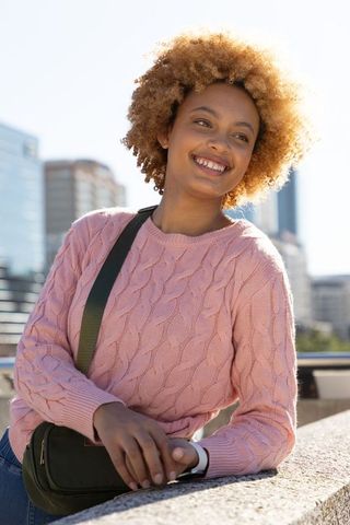 African american woman leaning on bridge ledge smiling in pink sweater