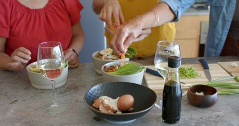 Multigenerational women preparing fresh salad bowls with senior woman in yellow apron