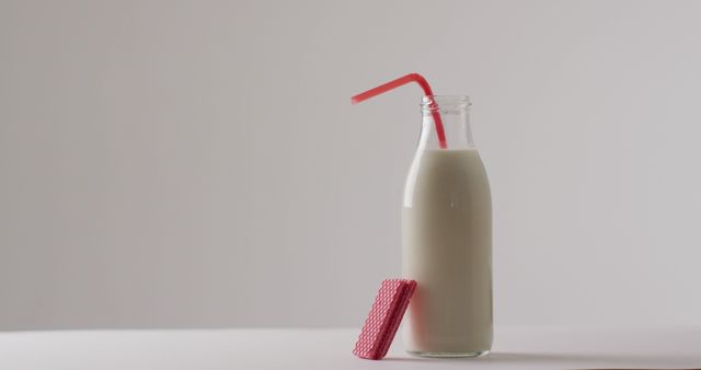 Milk bottle featuring a pink straw and a pink wafer snack placed next to it in front of plain white background. Useful for illustrating healthy breakfast, minimalist food settings, dairy products, simple lifestyle, or dessert presentations.