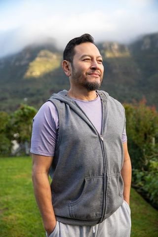 Mature asian man enjoying serene misty mountain morning with hands in pockets