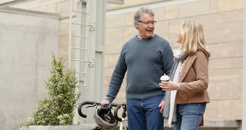Mature couple enjoying relaxed urban stroll with bicycle helmet and takeaway coffee