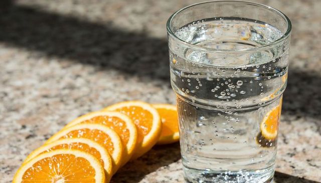 Sparkling water glass with rising bubbles and sliced oranges on granite countertop