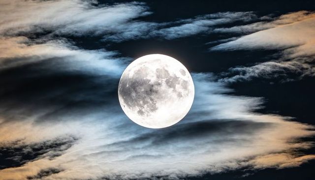 Glowing full moon revealing lunar maria and craters amid layered clouds in night sky