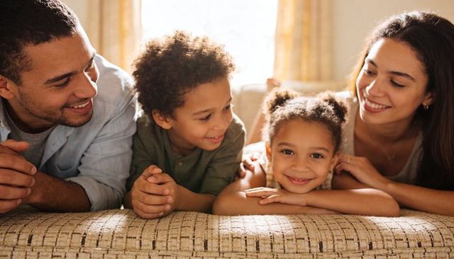 Smiling family relaxing on sunlit sofa sharing warm moment in cozy living room
