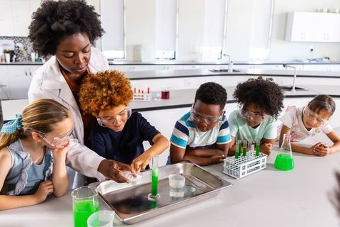 African american teacher guiding students during hands-on chemistry experiment with safety goggles