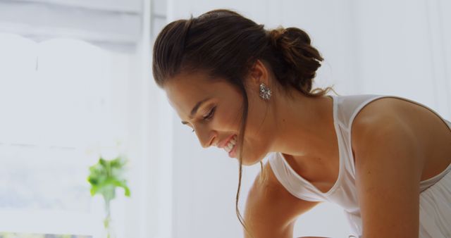 This image depicts a young woman in an elegant white dress, smiling and looking downwards. The bright, minimalistic background enhances the focus on her cheerful expression. Suitable for use in lifestyle blogs, fashion magazines, or advertising campaigns focusing on beauty, elegance, or joy.