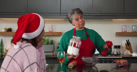 Multigenerational women baking holiday treats in cozy kitchen, measuring flour and smiling