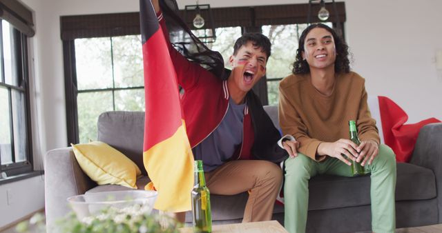 Two enthusiastic friends sit on a couch watching a sports match. One of the friends is energetically cheering and holding a German flag, while the other casually holds a beer bottle and looks onward. The scene suggests a lively and engaging atmosphere perfect for illustrating themes of friendship, celebration, sports fandom, and leisure activities.