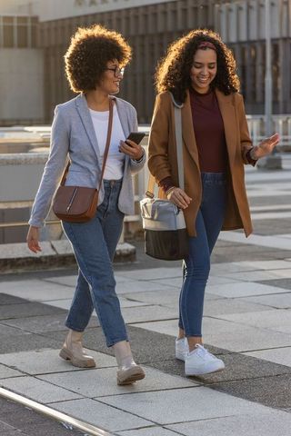 Two friends walking and chatting in urban plaza wearing blazers and jeans